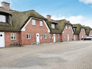 Une rangée de maisons en briques rouges, avec des toits de chaume et des éléments décoratifs blancs, une allée gravillonnée et une voiture garée.