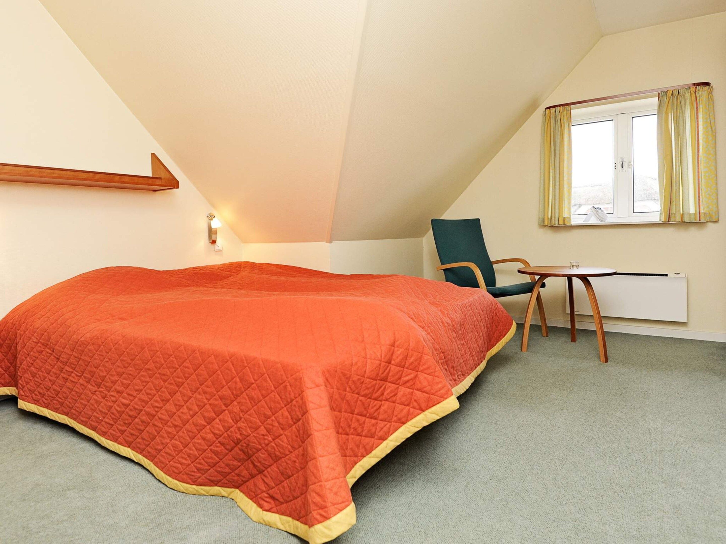 Ein Schlafzimmer mit einem Bett, einem Sessel, einem Schreibtisch und einem Fenster mit Vorhängen.