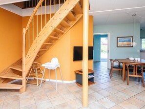 A spacious room with a wooden staircase, a dining area with a table and chairs, and a television mounted on the wall. - 4 Star Holiday Home in Blavand (Blavand)