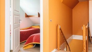 Una stanza con una scala in legno, un letto con biancheria rossa e una porta bianca.