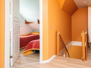 A room with a wooden staircase, a bed with red bedding, and a white door. - 4 Star Holiday Home in Blavand (Blavand)