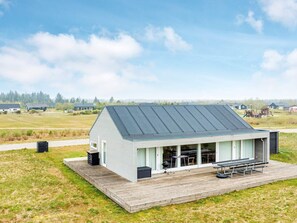 A single-story building with a flat roof, a covered patio area with picnic tables, and a grill. - 8 Person Holiday Home in Brovst-by Traum (Brovst)