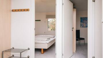 A bedroom with a bed, a wooden floor, a metal drying rack, and a window with a view of trees.