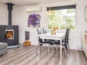 A modern interior with a wood-burning stove, a dining table with chairs, and a large window with a view of greenery. - 6 Person Holiday Home in Kolind-by Traum (Kolind)