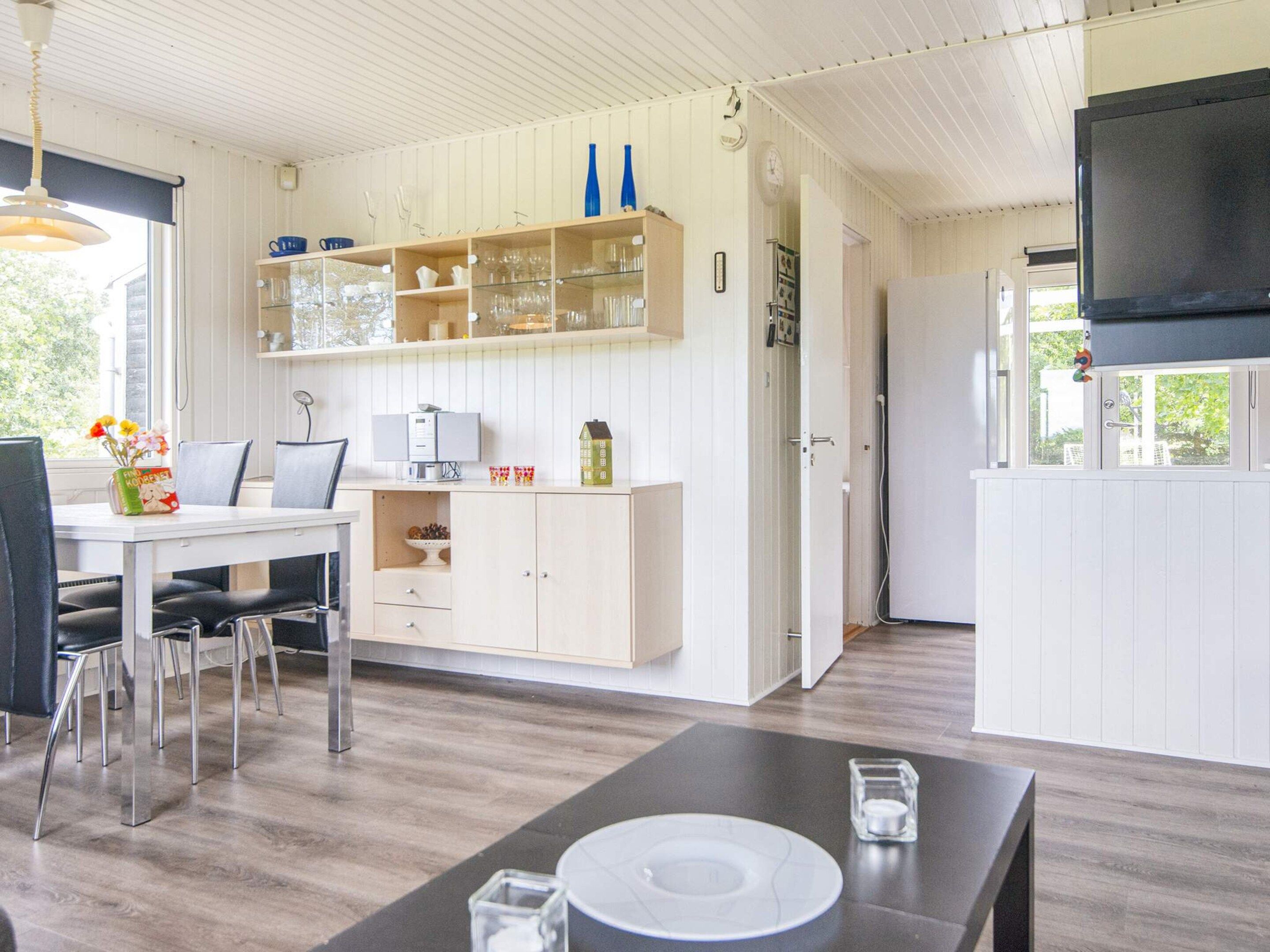A modern kitchen with white cabinetry, a dining area with a table and chairs, and a television mounted on the wall.