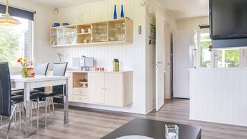 A modern kitchen with white cabinetry, a dining area with a table and chairs, and a television mounted on the wall.