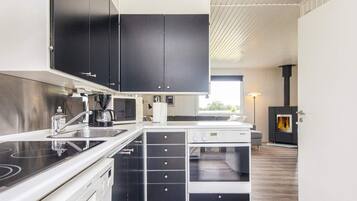 A modern kitchen with black cabinets, a white countertop, a built-in stove, and a wood-burning stove.