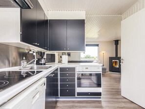 A modern kitchen with black cabinets, a white countertop, a built-in stove, and a wood-burning stove. - 6 Person Holiday Home in Kolind-by Traum (Kolind)