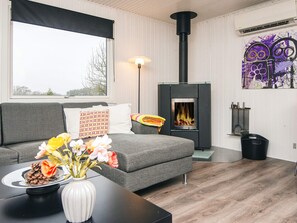 A living room with a sofa, a table with a vase of flowers, a fireplace, and a wall with a piece of abstract art. - 6 Person Holiday Home in Kolind-by Traum (Kolind)