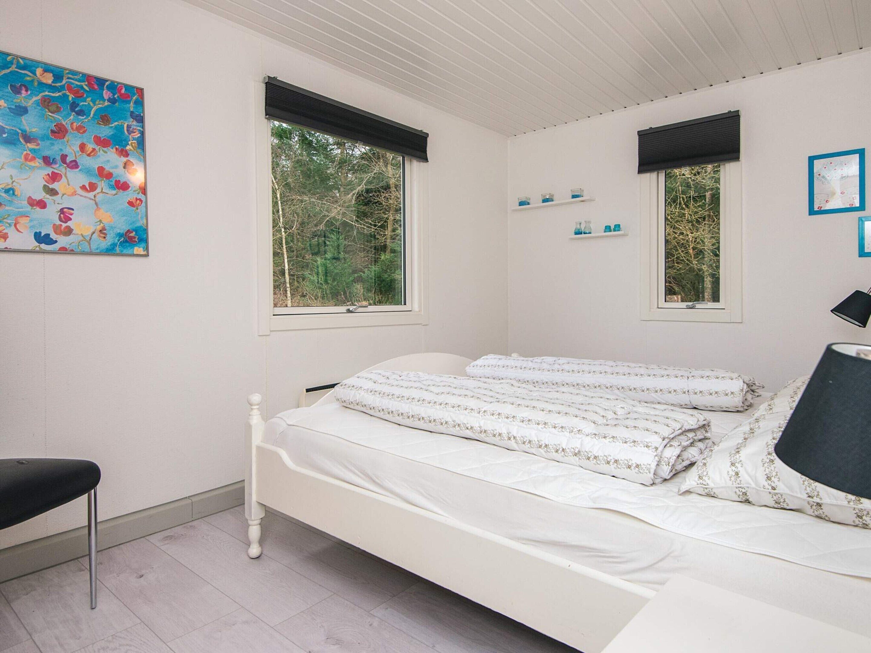 A bedroom with a bed, two windows, a chair, and a painting.