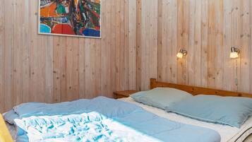 A bedroom with a wooden wall, a bed with blue bedding, a painting, and two wall-mounted lamps.