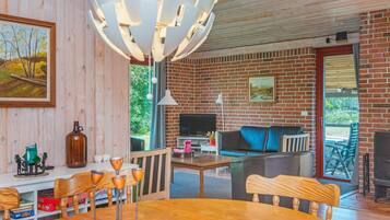 A cozy living room with a brick wall, a television, a sofa, and a dining area with a table and chairs.