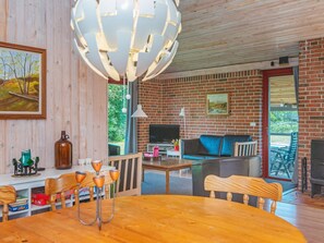 Uma sala de estar aconchegante com parede de tijolos, televisão, sofá e um espaço de refeições com mesa e cadeiras.