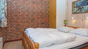 Quarto com parede de tijolos, estrutura de cama de madeira, luminária verde fixada na parede e pintura de veados.