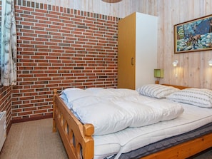 A bedroom with a brick wall, a wooden bed frame, a green wall-mounted lamp, and a painting of deer. - 6 Person Holiday Home in Orsted-by Traum (Ørsted)