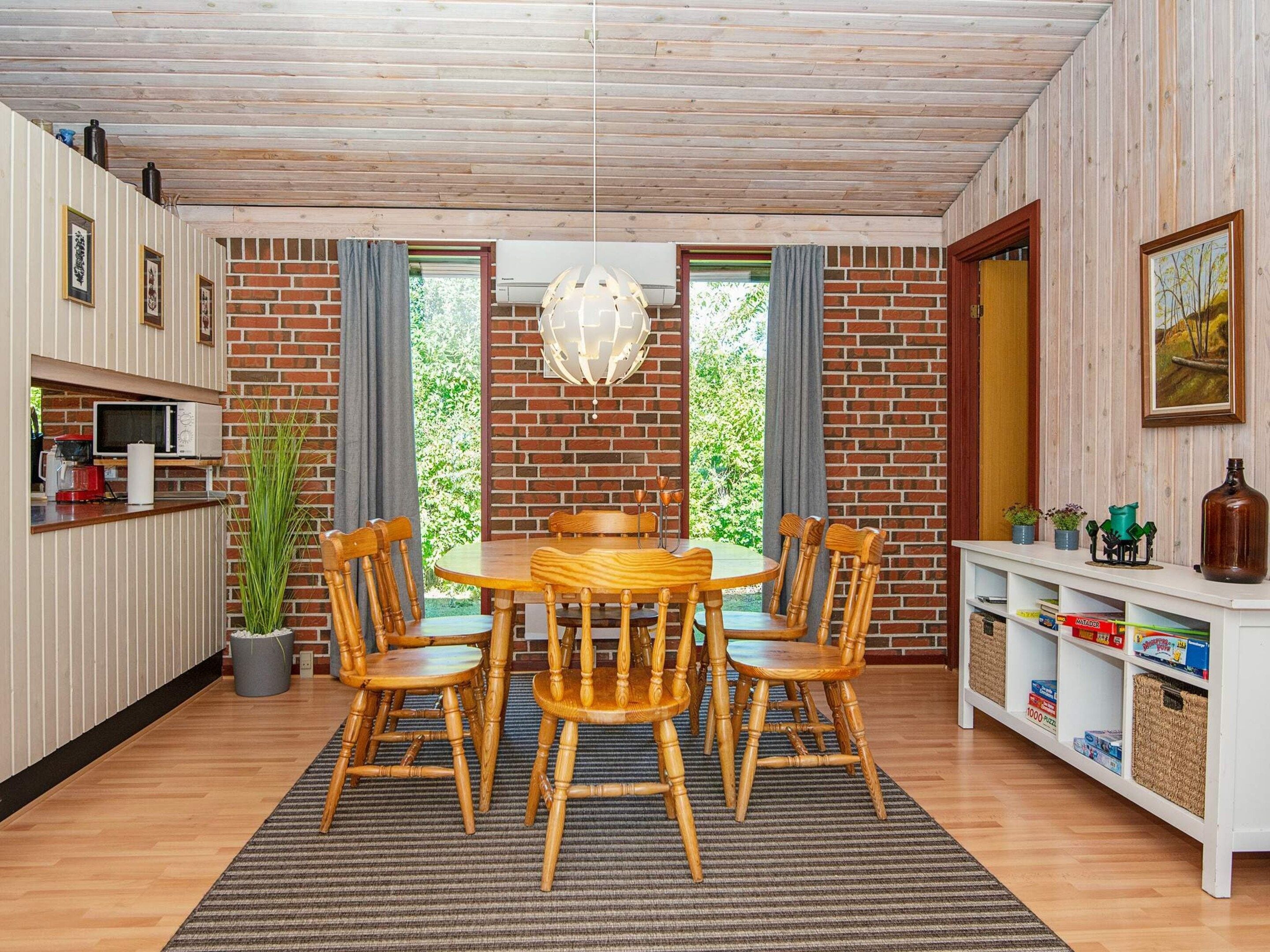 A dining area with a wooden table and chairs, a hanging light fixture, and a brick wall.