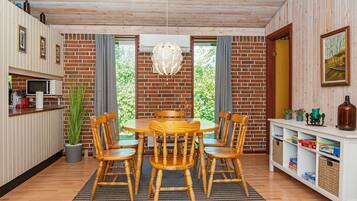A dining area with a wooden table and chairs, a hanging light fixture, and a brick wall.