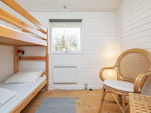 A compact room with a bunk bed, a single chair, a table, a window, and a radiator.