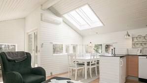 A spacious room with a high ceiling, a skylight, a dining area with a white table and chairs, a kitchen with white cabinets, and a dark green armchair. - 5 Person Holiday Home in Albaek (Aalbaek)