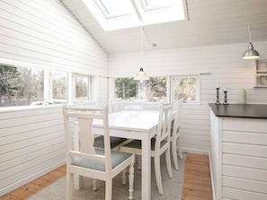 A white interior with a skylight, a dining table with chairs, and a kitchen area.