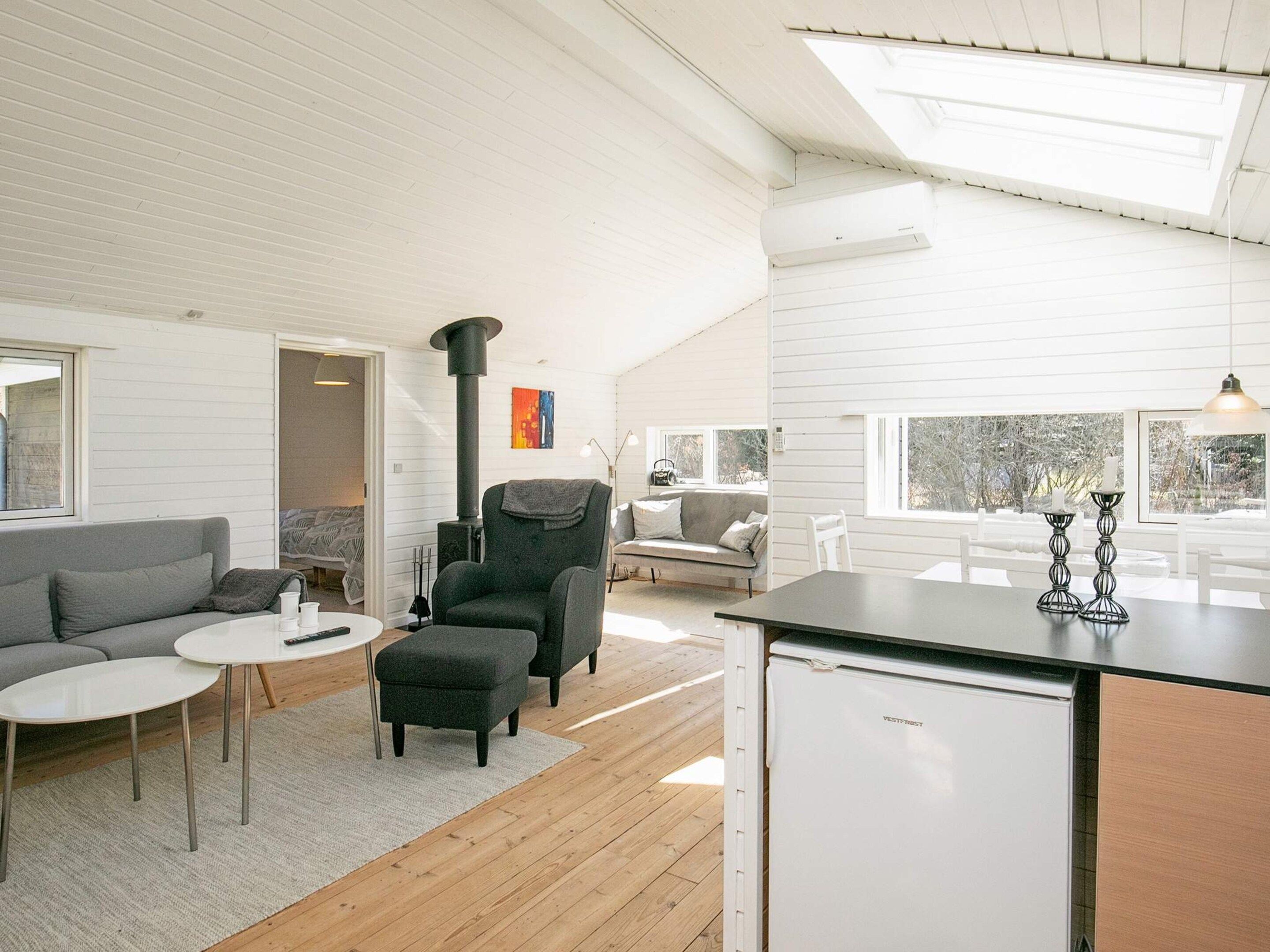 A modern interior with a kitchen area, a seating area with a sofa and ottoman, and a large window providing a view.