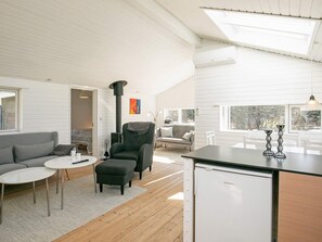 A modern interior with a kitchen area, a seating area with a sofa and ottoman, and a large window providing a view.