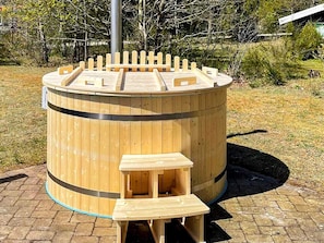 A wooden hot tub with a bench and a small table in a landscaped area. - 4 Star Holiday Home in Glesborg (Glesborg)