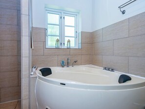A bathroom with a large bathtub, a window with two small stools, and a towel rack. - 4 Star Holiday Home in Glesborg (Glesborg)