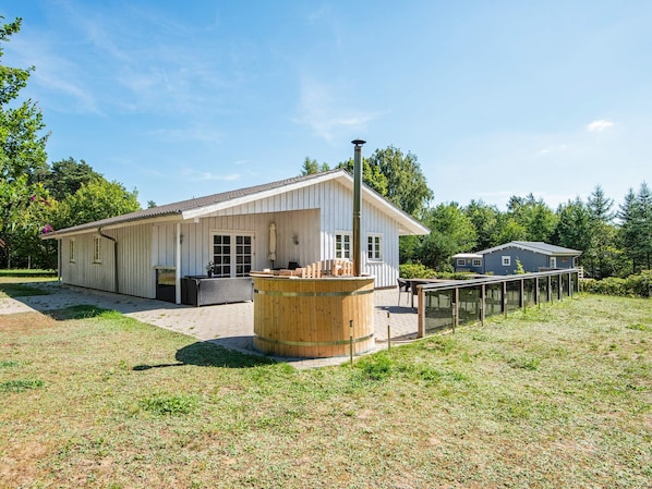 A single-story building with a covered patio area, a wooden barrel, and a fenced outdoor space. - 4 Star Holiday Home in Glesborg (Glesborg)