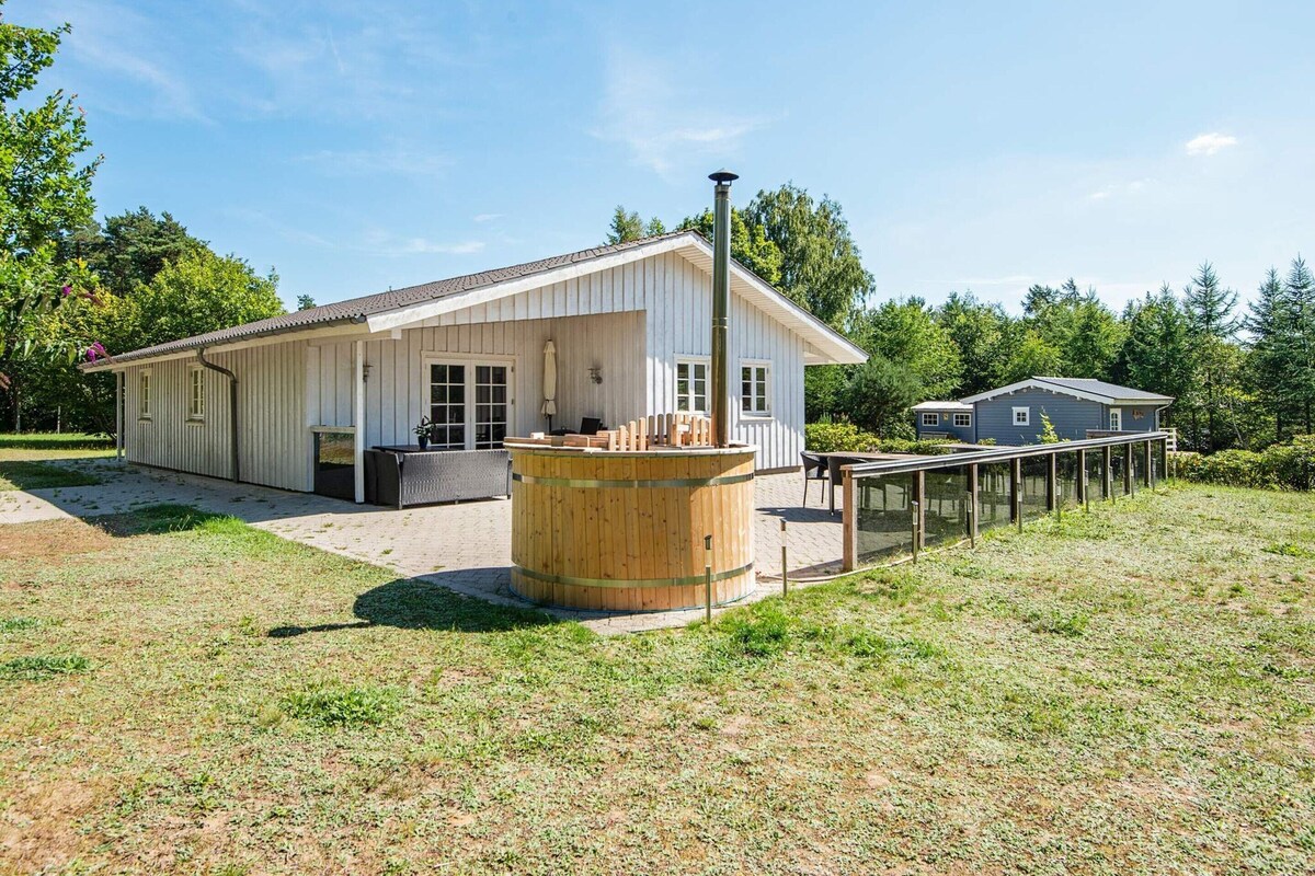 A white building with a covered patio, a wooden barrel, and a small house in the background.