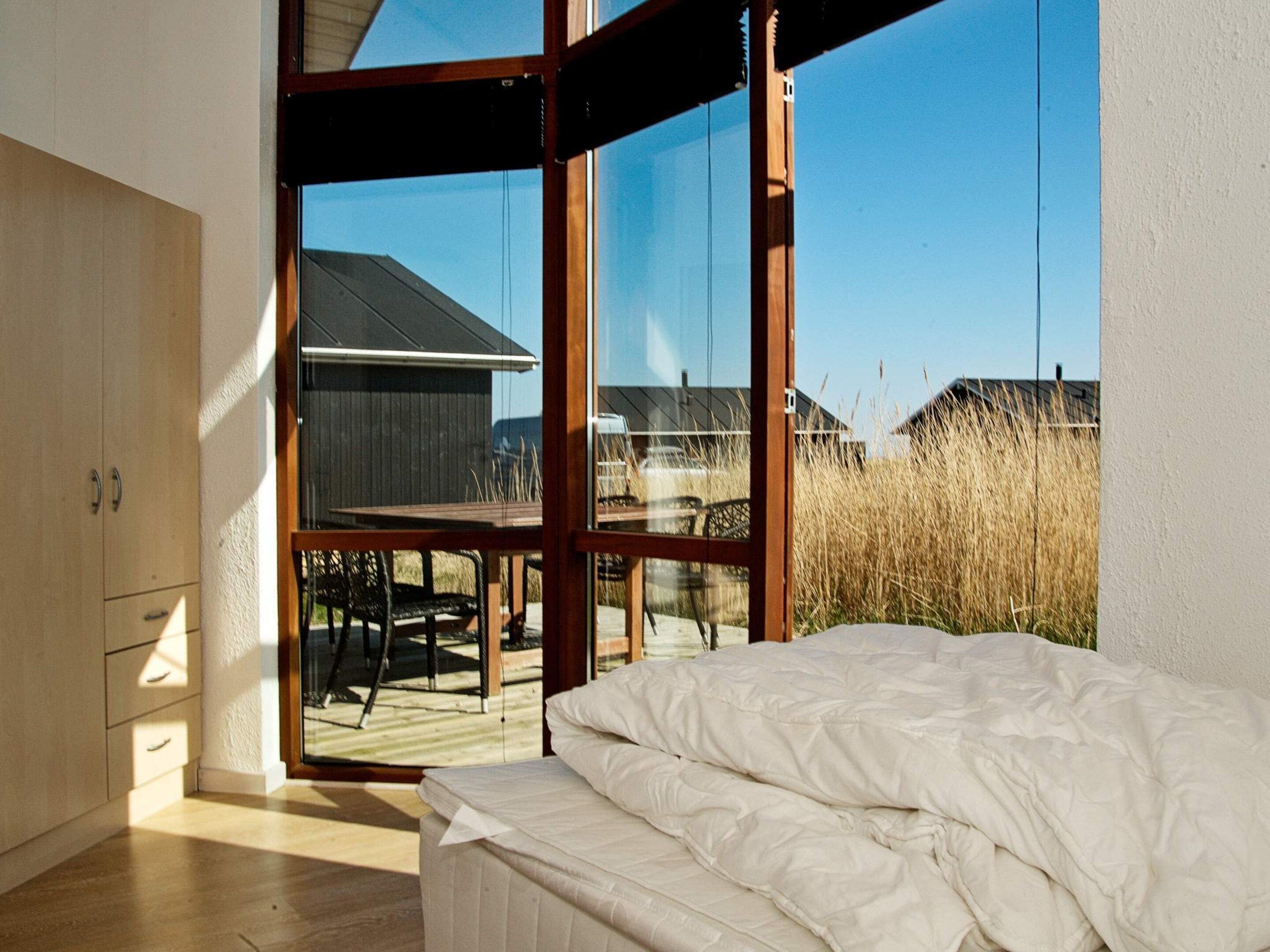 A bedroom with a large window, a bed, and a wooden wardrobe.