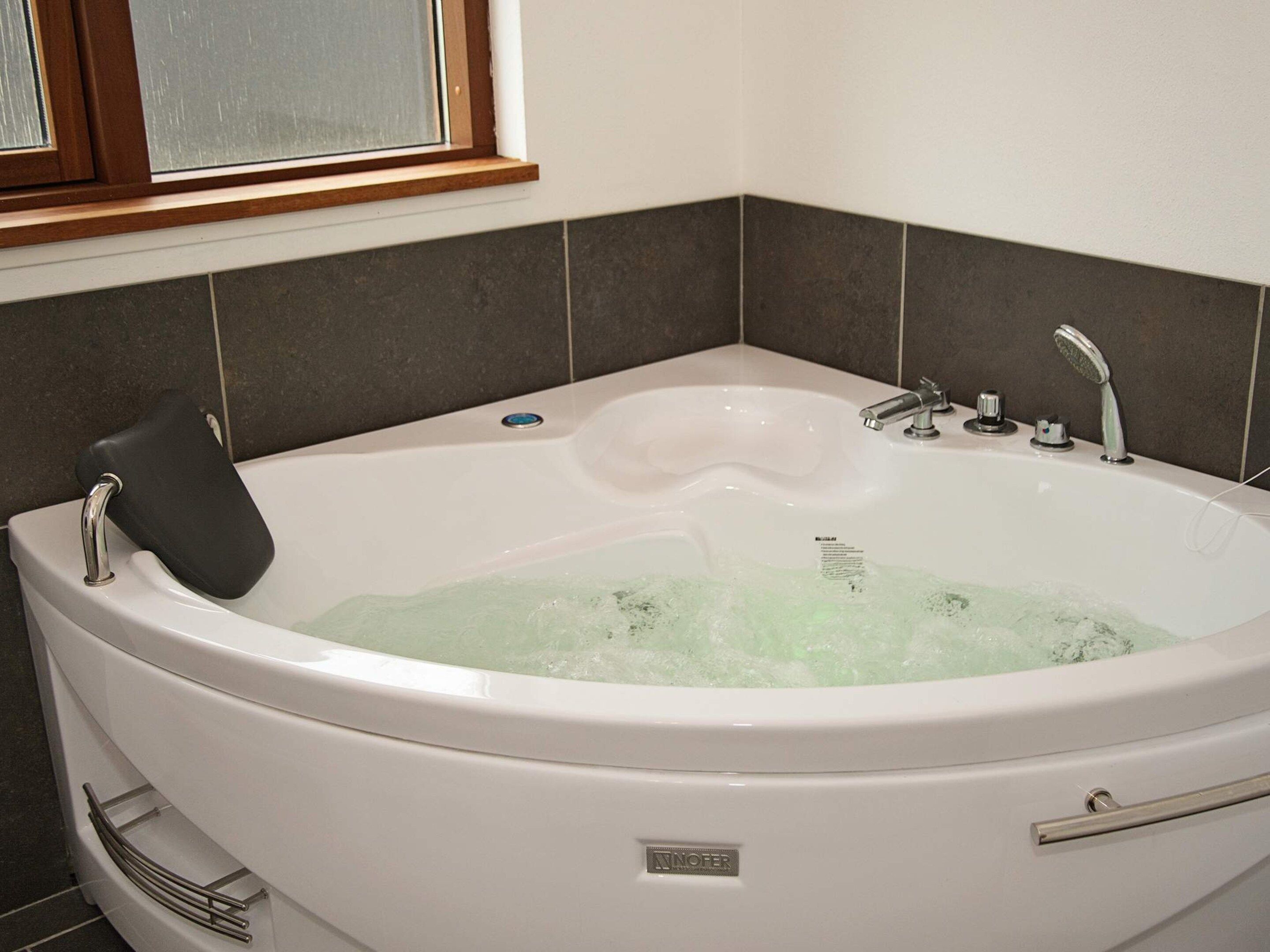 Una bañera blanca con un asiento negro, un cabezal de ducha manual y una perilla de control.