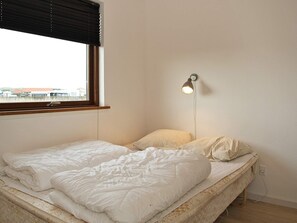 Un lit simple avec une tête de lit, une lampe de chevet et une fenêtre avec des stores.
