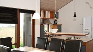 A modern kitchen with a dining area, featuring a large island, black chairs, and pendant lighting.