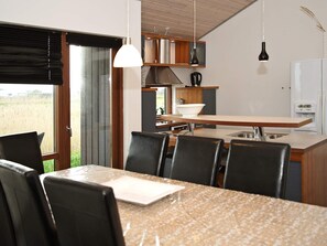 A modern kitchen with a dining area, featuring a large island, black chairs, and pendant lighting. - 8 Person Holiday Home in Ulfborg (Ulfborg)