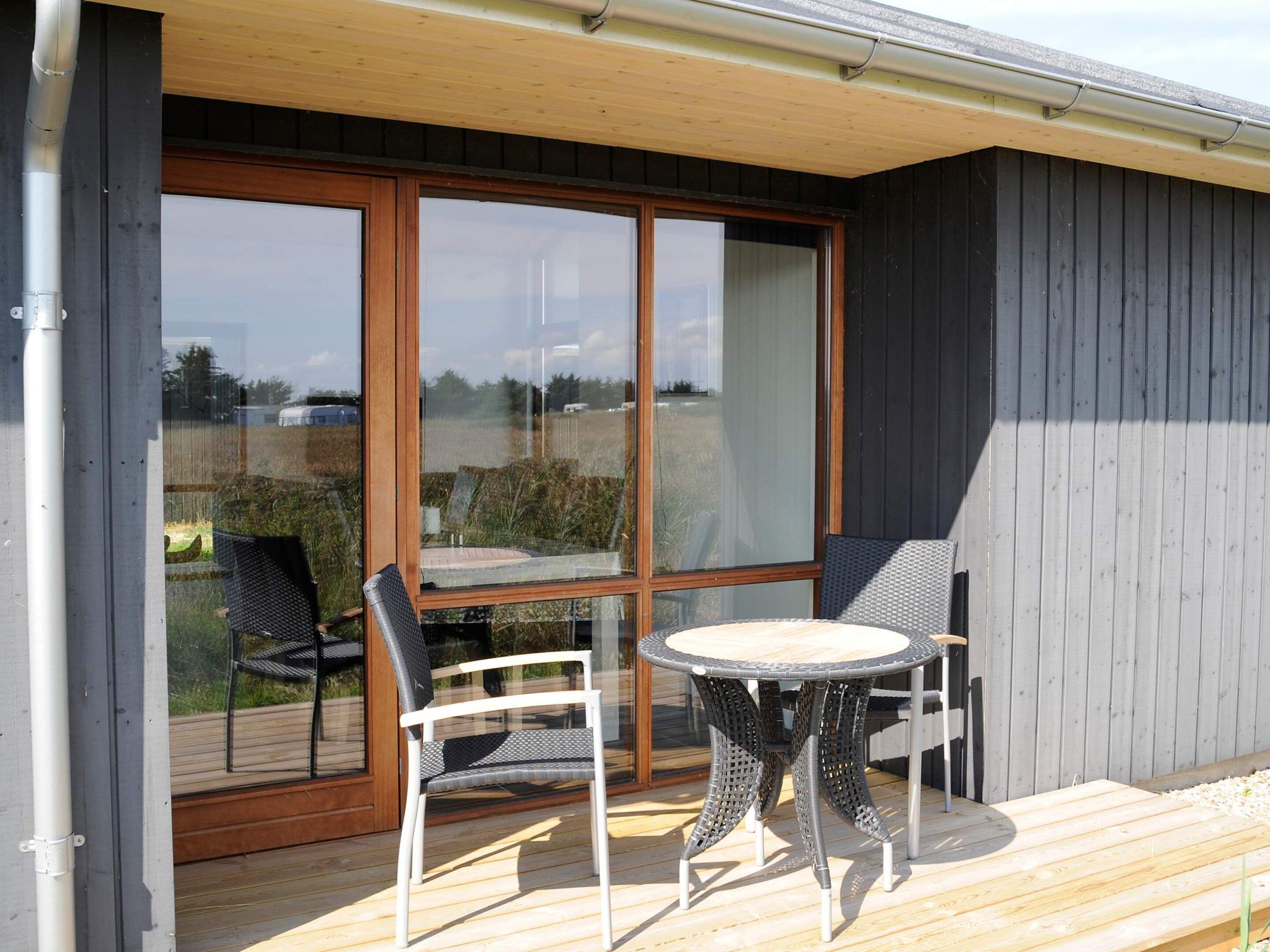 Une terrasse avec une table et des chaises, une plateforme en bois et une grande porte-fenêtre coulissante donnant sur un espace extérieur.