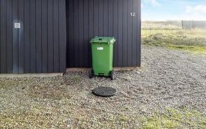 A green dumpster next to a building with a door marked with the number 12.