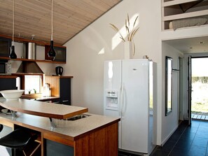 A modern kitchen with a white refrigerator, wooden cabinets, and a large island with a sink. - 8 Person Holiday Home in Ulfborg (Ulfborg)