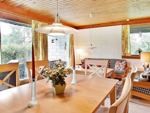 A cozy dining area with a wooden table, chairs, and a vase of flowers. There are hanging lights and a brick wall in the background. - Rustic Holiday Home in Asnæs near Sea (Asnaes)