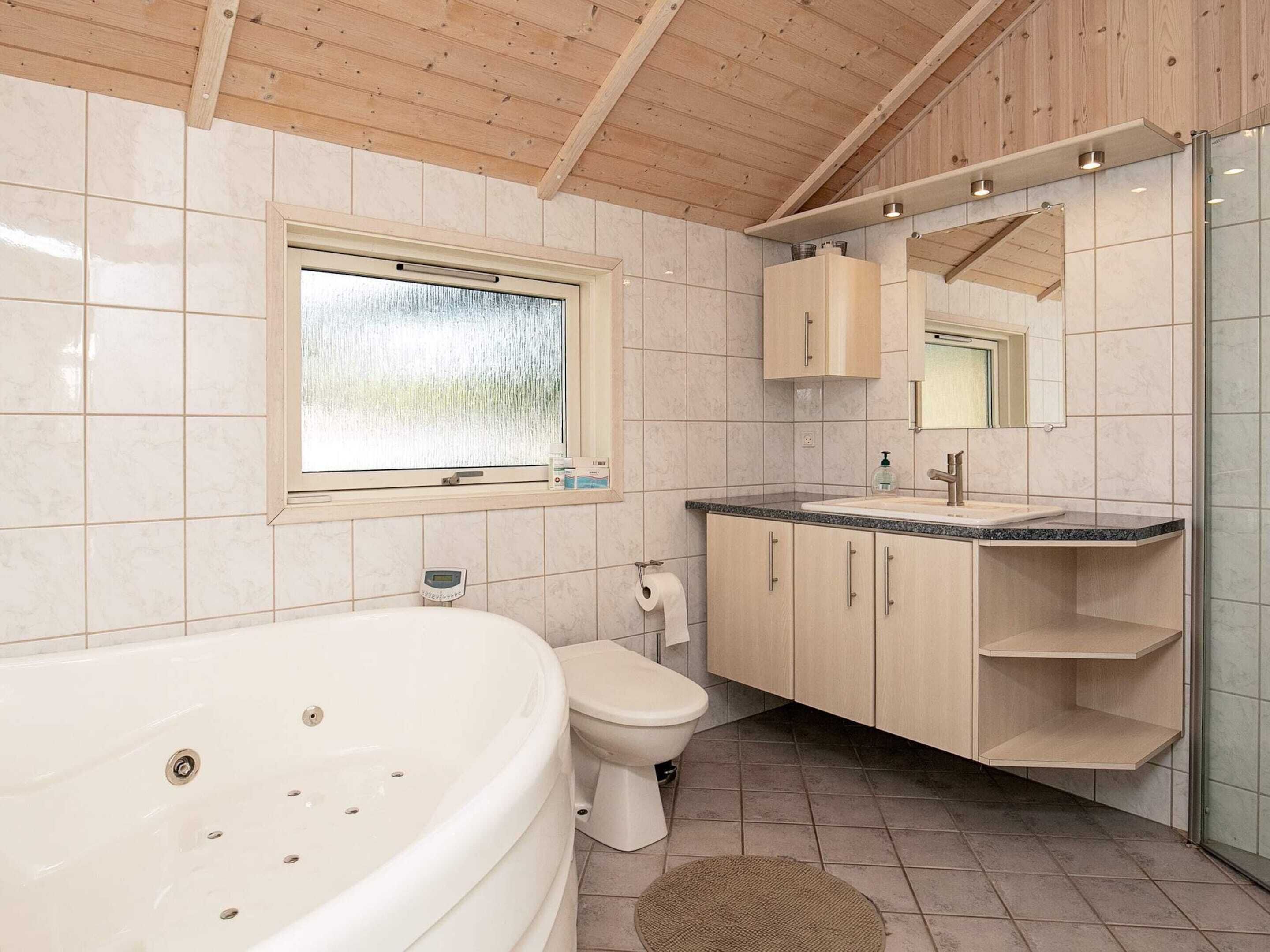 Ein modernes Badezimmer mit freistehender Badewanne, Toilette, Waschtisch und Spiegel sowie einem Fenster über dem Waschbecken.