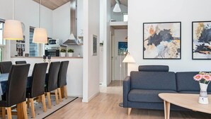 A modern living room with a grey sofa, a dining area with a table and chairs, and abstract art on the wall. - 8 Person Holiday Home in Brovst (Brovst)