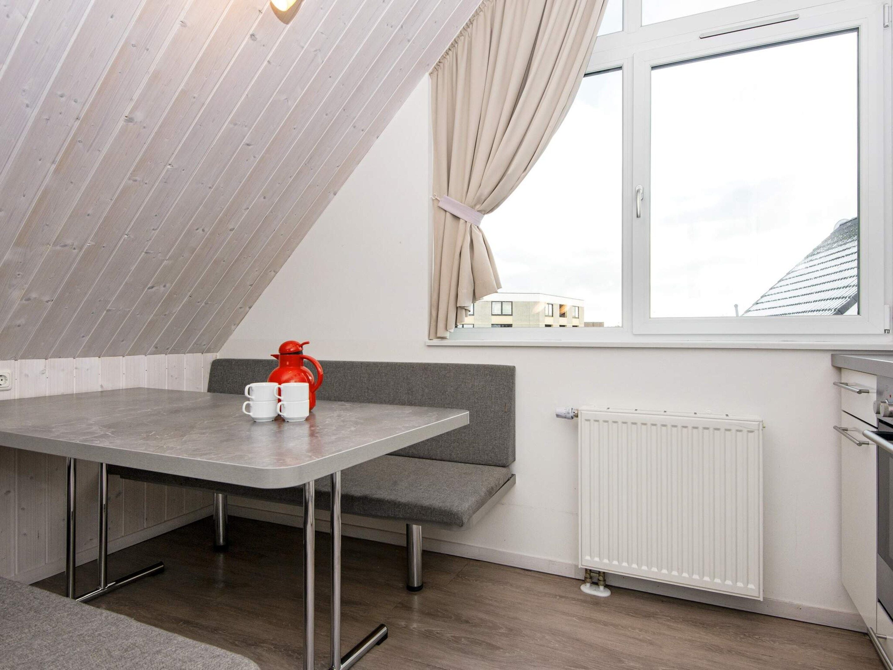 A small kitchenette with a window, a radiator, and a table with cups and a kettle.