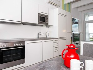 Una cocina moderna con horno empotrado, microondas y tetera roja sobre la encimera.