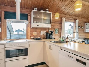 A modern kitchen with white cabinetry, a built-in oven, a coffee maker, and a window with a view of a house. - 6 Person Holiday Home in Hirtshals (Hirtshals)