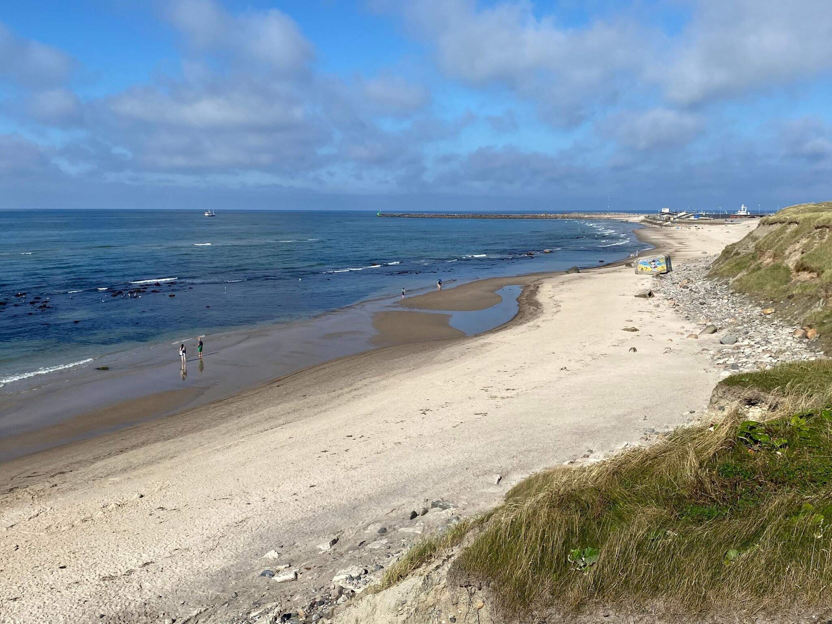 Een kuststrand met een zandstrand, een grasheuvel en een heldere lucht.