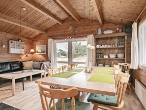 A cozy cabin interior with a wooden dining table, chairs, a sofa, and a kitchen area with shelves. - 6 Person Holiday Home in Hirtshals (Hirtshals)