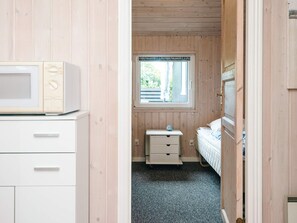 A bedroom with a wooden floor, a window with a view of greenery, a bed, a bedside table with a clock, and a microwave on a cabinet. - 6 Person Holiday Home in Hemmet (Hemmet)
