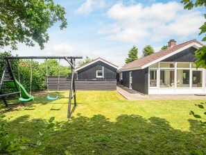 A residential backyard with a swing set, a slide, a fenced area, and a house with large windows. - 6 Person Holiday Home in Hemmet (Hemmet)