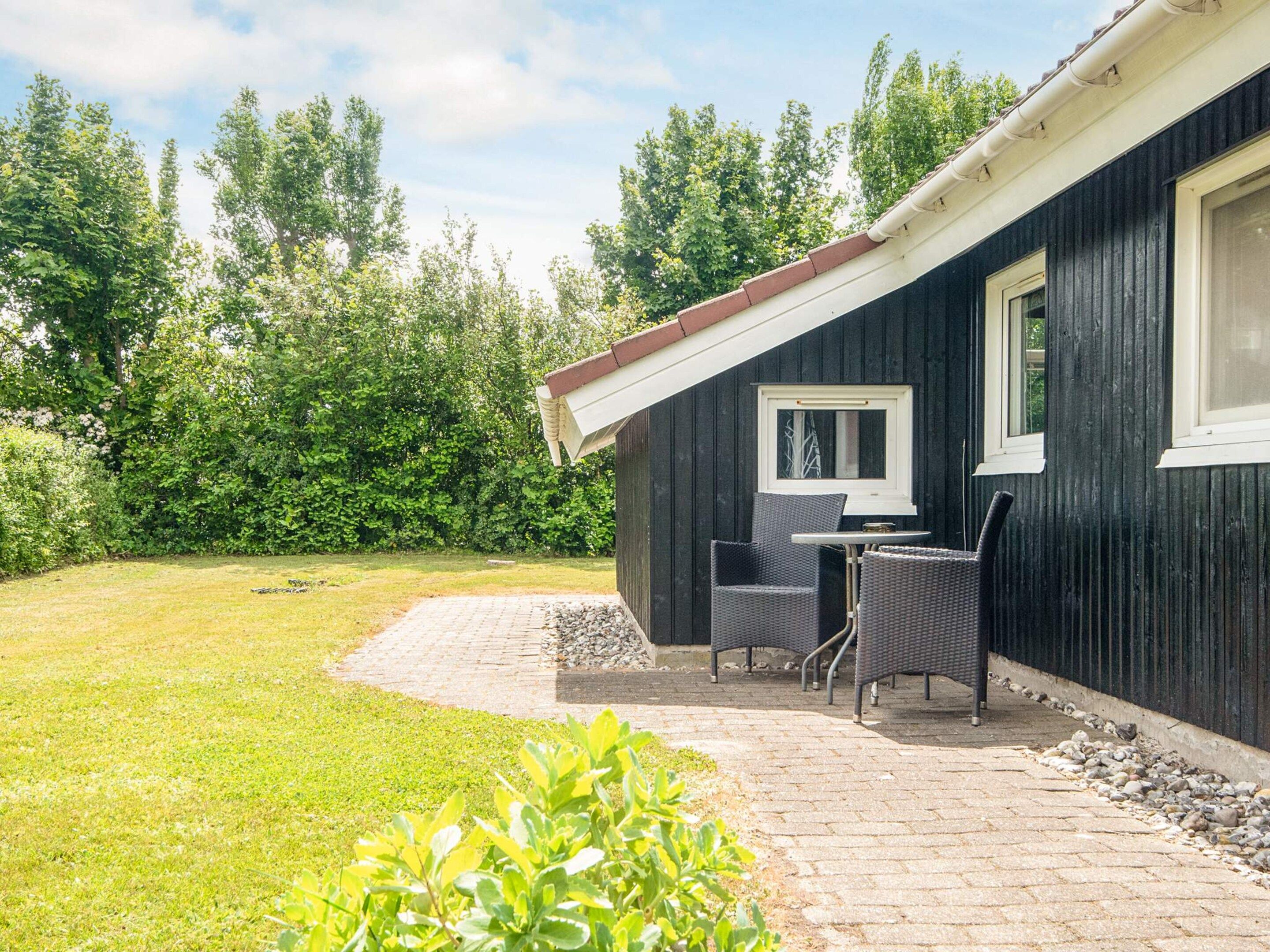A black building with a patio area featuring a table and chairs, surrounded by a grassy lawn and trees.
