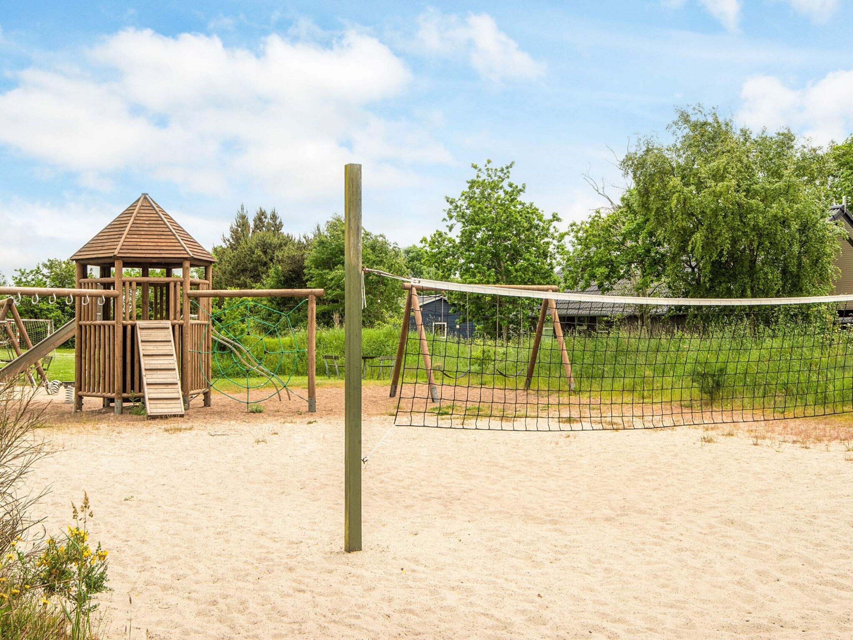 Un parque infantil con un juego de madera, una red de voleibol y una zona de arena.